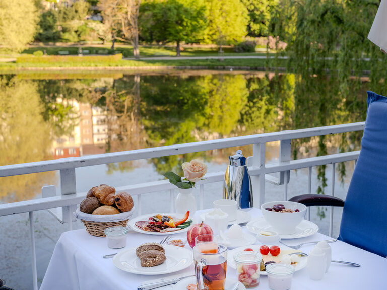 Gedeckter Tisch auf der Terrasse mit Speisen vom Frühstücksbuffet und Blick auf den See im Hotel Seehof Berlin