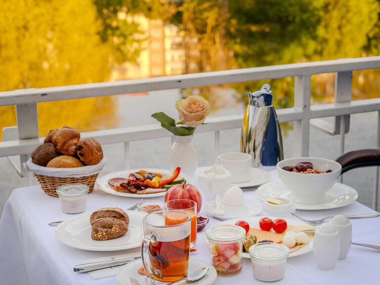Gedeckter Tisch auf der Terrasse mit Speisen vom Frühstücksbuffet und Blick auf den See im Hotel Seehof Berlin