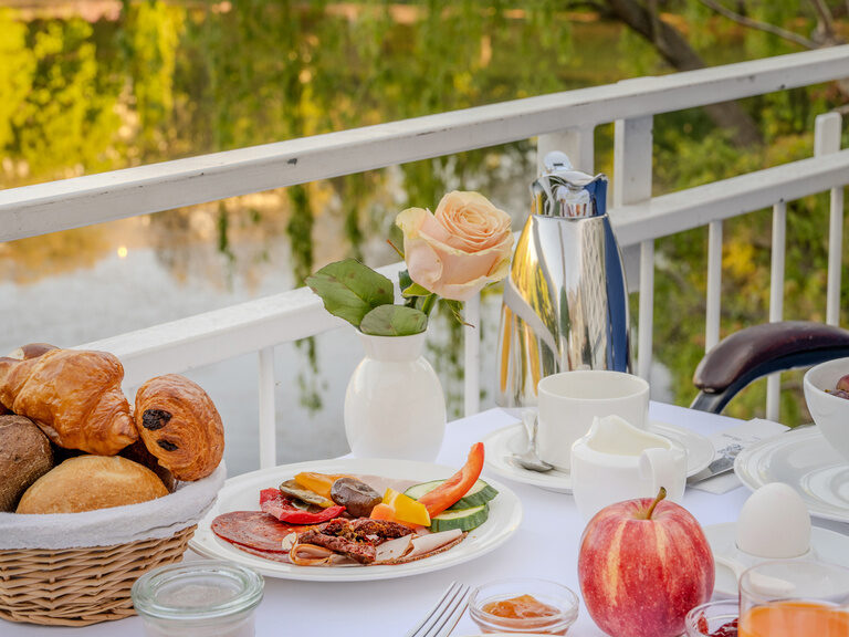 Gedeckter Tisch auf der Terrasse mit Speisen vom Frühstücksbuffet und Blick auf den See im Hotel Seehof Berlin