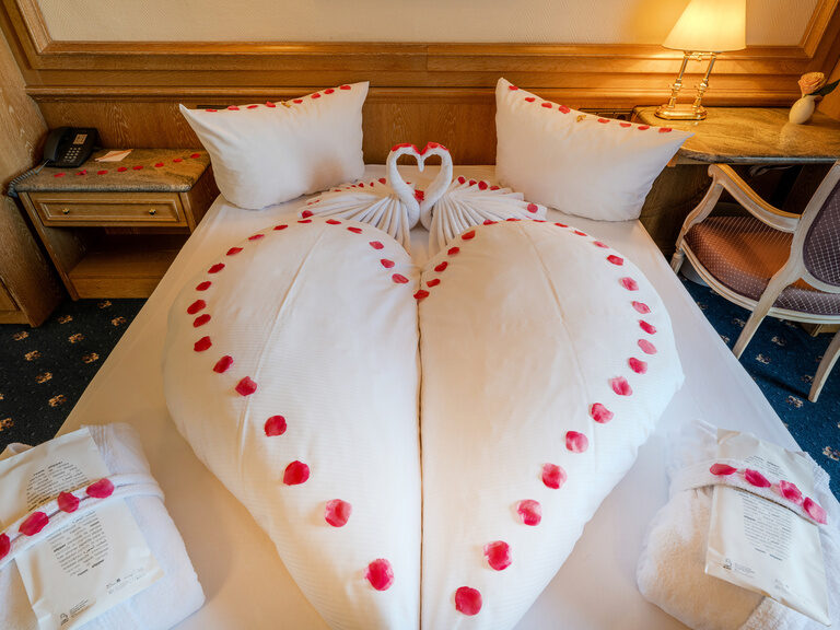 Aufnahme vom liebevoll hergerichtetem Bett mit Rosenblättern in einem romatisch dekorierten Zimmer im Ringhotel Seehof Berlin
