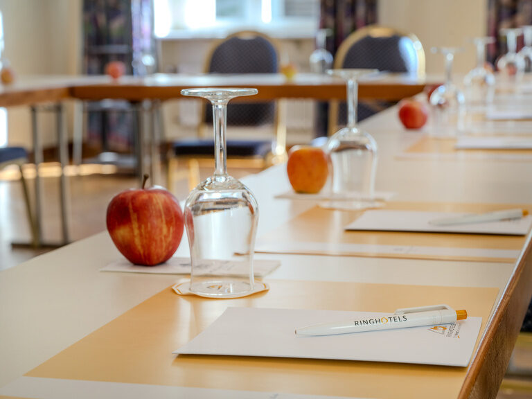 Nahaufnahme vom eingedeckten Platz mit Schreibunterlage, Apfel und Glas im Tagungsraum Kant in U-Form gestellt im Ringhotel Seehof Berlin